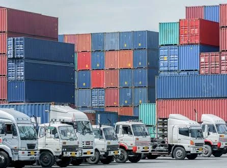 Trucks lined up in front of stacked shipping containers
